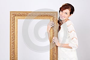 Beautiful woman in dress holds big gilt frame.