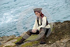 Beautiful woman dress like a pirate sitting on the seashore. Nice wave behind