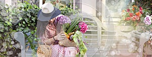 Beautiful woman in a dress with purchases, sits on a bench in the city street. A large basket of vegetables and flowers in the