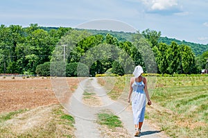 Beautiful woman in dress is walking the road in field