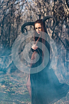 Beautiful woman dressed as a fairy witch in raincoat and with horns for Halloween