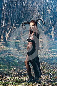 Beautiful woman dressed as a fairy witch in raincoat and with horns for Halloween