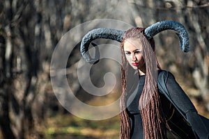Beautiful woman dressed as a fairy witch in raincoat and with horns for Halloween