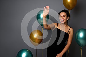 Beautiful woman dressed in elegant black evening dress stands against a gray wall background with golden and green metallic