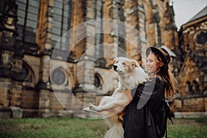 Beautiful woman, dressed elegantly, embracing her red border collie dog. Church in Gothic style on the background