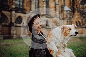 Beautiful woman, dressed elegantly, embracing her red border collie dog. Church in Gothic style on the background