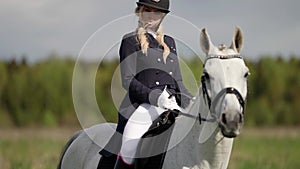 beautiful woman dressed like professional jockey is riding white horse at nature