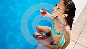 Beautiful woman drinking cocktail and sunbathing at pool