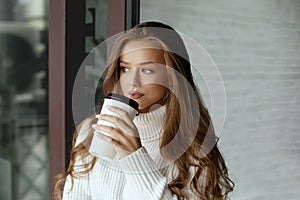 Beautiful woman drinking coffee. Girl holds paper cup of hot coffee.