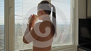 Beautiful woman drinking coffee and opening window blinds. People in morning, beautiful cityscape, having break at office