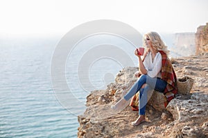 Beautiful woman drinking coffee sitting on the rocky shore