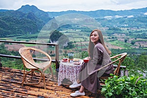 A beautiful woman drinking hot coffee on balcony with mountains and green nature background