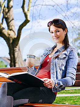 Krásná žena pití a čtení na lavice 