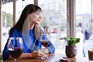 Beautiful woman drinking red wine with friends in restaurant, portrait with wine glass near window. Vocation holidays bar concept