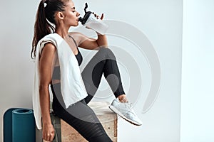 Beautiful woman drinking some water from plastic bottle after fitness