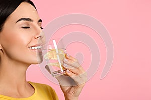 Beautiful woman drinking tasty lemon water on pink background, closeup. Space for text