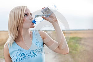 Beautiful woman drinking water from bottle while standing on field