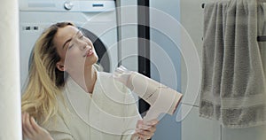 Beautiful woman drying hair with hairdryer after taking shower in bathroom. Concept of well-groomed and beautiful woman.