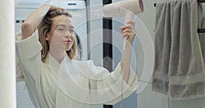 Beautiful woman drying hair with hairdryer after taking shower in bathroom. Concept of well-groomed and beautiful woman.