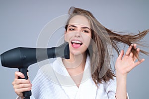 Beautiful woman drying her hair with a hairdryer isolated on studio background. Young woman with blow dryer drying hair