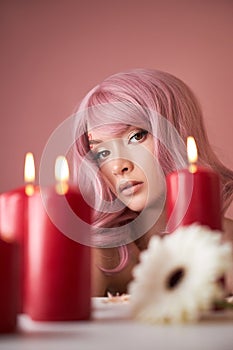 Beautiful woman with dyed pink hair guessing at flower in hand at table with candles. Pink beauty hair on head of woman fortune