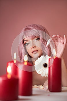 Beautiful woman with dyed pink hair guessing at flower in hand at table with candles. Pink beauty hair on head of woman fortune