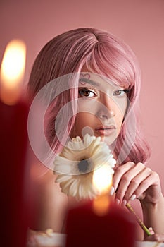 Beautiful woman with dyed pink hair guessing at flower in hand at table with candles. Pink beauty hair on head of woman fortune