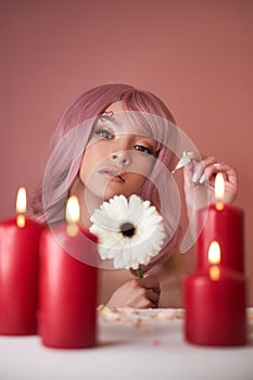 Beautiful woman with dyed pink hair guessing at flower in hand at table with candles. Pink beauty hair on head of woman fortune