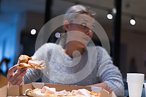 Beautiful woman eating pizza and drinking cola while sitting inside expres restaurant late at night