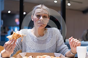 Beautiful woman eating pizza and drinking cola while sitting inside expres restaurant late at night