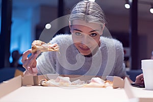 Beautiful woman eating pizza and drinking cola while sitting inside expres restaurant late at night