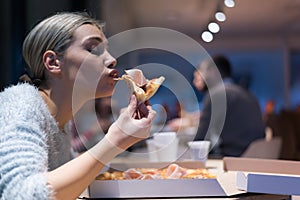 Beautiful woman eating pizza and drinking cola while sitting inside expres restaurant late at night