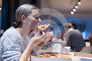 Beautiful woman eating pizza and drinking cola while sitting inside expres restaurant late at night