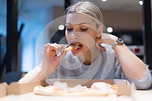 Beautiful woman eating pizza and drinking cola while sitting inside expres restaurant late at night