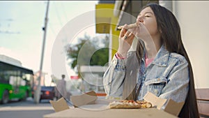 Beautiful woman eating pizza on street. Media. Woman snacking on pizza for lunch outside cafe. Young woman eats pizza on