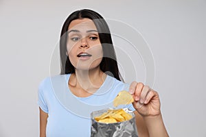 Beautiful woman eating potato chips on grey background