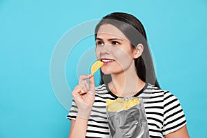 Beautiful woman eating potato chips on light blue background. Space for text