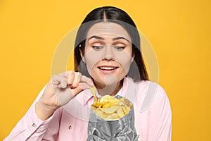 Beautiful woman eating potato chips on orange background