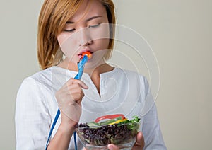 Beautiful woman eating salad with fork tape measure wrapped.