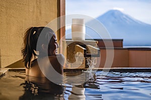 Beautiful woman enjoy onsen mineral hot bath in morning and seeing view of Fuji mountain in japan