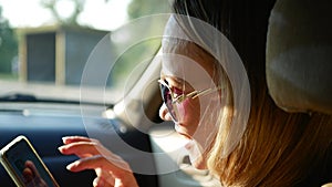 Beautiful woman enjoy the trip in the car. Girl passenger in the front seat with a mobile phone in the daytime. Holidays