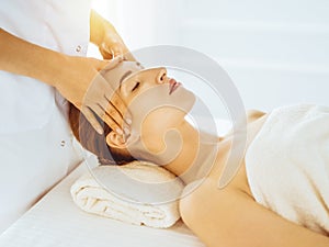 Beautiful woman enjoying facial massage with closed eyes in sunny spa center. Relaxing treatment concept in medicine