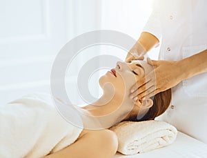 Beautiful woman enjoying facial massage with closed eyes in sunny spa center. Relaxing treatment concept in medicine