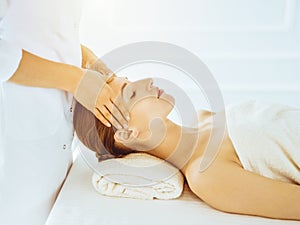 Beautiful woman enjoying facial massage with closed eyes in sunny spa center. Relaxing treatment concept in medicine