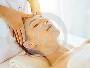 Beautiful woman enjoying facial massage with closed eyes in sunny spa center. Relaxing treatment concept in medicine