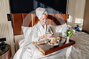 Beautiful woman enjoying her morning breakfast in comfortable bed. Hotel Room Service concept.