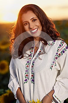 Beautiful woman enjoying nature in the sunflower field at sunset. Traditional clothes. Attractive brunette woman with long and