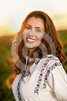 Beautiful woman enjoying nature in the sunflower field at sunset. Traditional clothes. Attractive brunette woman with long and