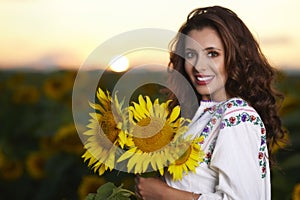 Beautiful woman enjoying nature in the sunflower field at sunset. Traditional clothes. Attractive brunette woman with long and