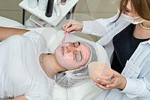 Beautiful woman enjoying rejuvenated pink clay face mask at spa salon